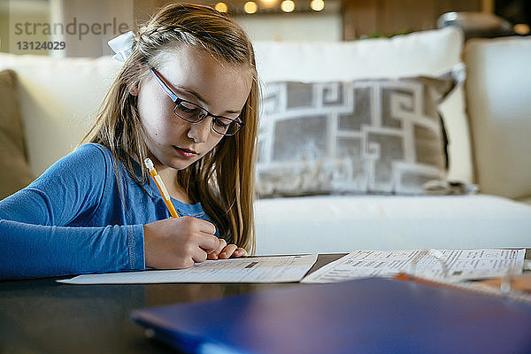 Seriöses Mädchen macht Hausaufgaben bei Tisch