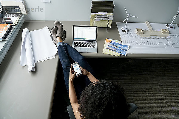 Weitwinkelansicht einer Geschäftsfrau  die ein Smartphone benutzt  während sie sich am Schreibtisch im Büro entspannt