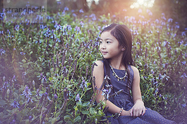 Süßes Mädchen schaut weg  während es inmitten blühender Pflanzen im Park sitzt