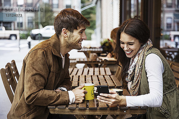 Mann sieht seine Freundin im Café mit dem Handy an