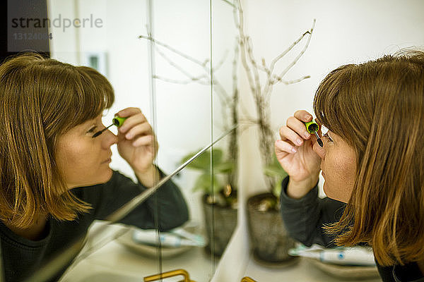 Nahaufnahme einer Frau  die Wimperntusche aufträgt  während sie sich zu Hause im Spiegel spiegelt