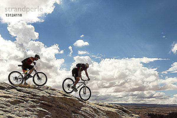 Seitenansicht von Mountainbikern auf Fahrrädern vor bewölktem Himmel