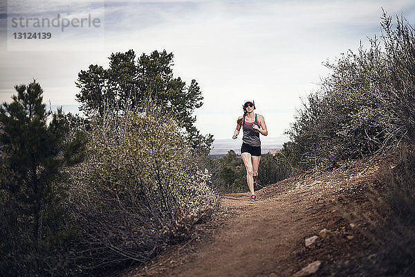 Sportliche Frau läuft in voller Länge auf Berg gegen Himmel