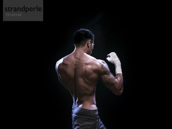 Rückansicht eines männlichen Kickboxers  der vor schwarzem Hintergrund trainiert