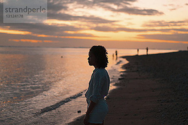 Seitenansicht einer Frau  die bei Sonnenuntergang am Strand vor bewölktem Himmel steht
