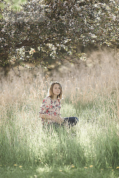 Porträt eines Mädchens  das auf einem Grasfeld unter einem Baum sitzt