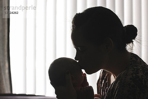 Mutter küsst neugeborene Tochter  während sie zu Hause sitzt