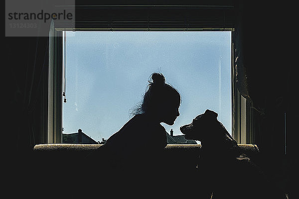 Mädchen und Hund sitzen auf dem Fensterbrett vor klarem Himmel