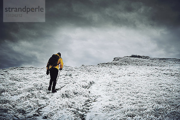 Rückansicht eines männlichen Wanderers  der auf einem schneebedeckten Berg vor bewölktem Himmel wandert