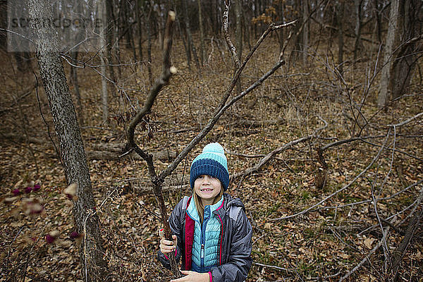 Hochwinkelporträt eines Mädchens  das einen getrockneten Ast hält  während es im Wald steht