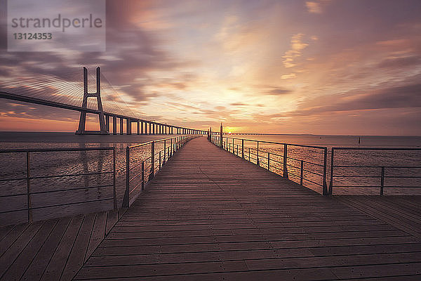 Strandpromenade an der Vasco-da-Gama-Brücke über den Tejo vor dramatischem Himmel bei Sonnenaufgang