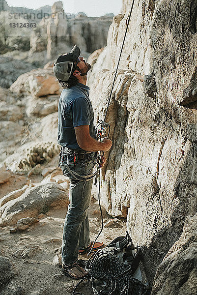 Wanderer schaut auf  während er das Kletterseil an einer Felsformation hält