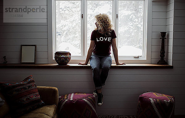 Eine Frau in voller Länge trägt ein T-Shirt mit dem Text LOVE  während sie zu Hause durch ein Fenster schaut