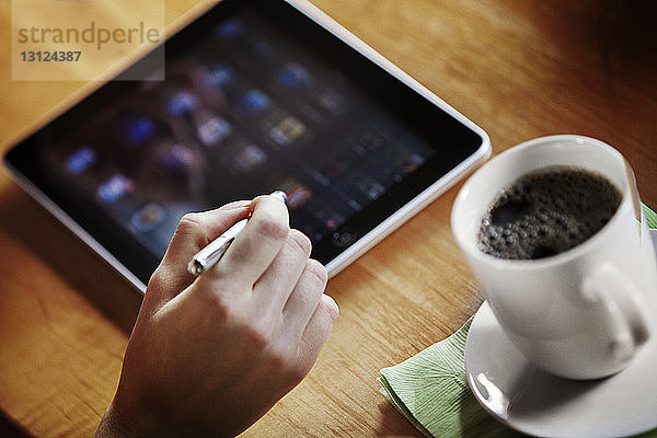 Ausgeschnittenes Bild eines handgehaltenen Stiftes und Verwendung eines digitalen Tabletts auf dem Tisch
