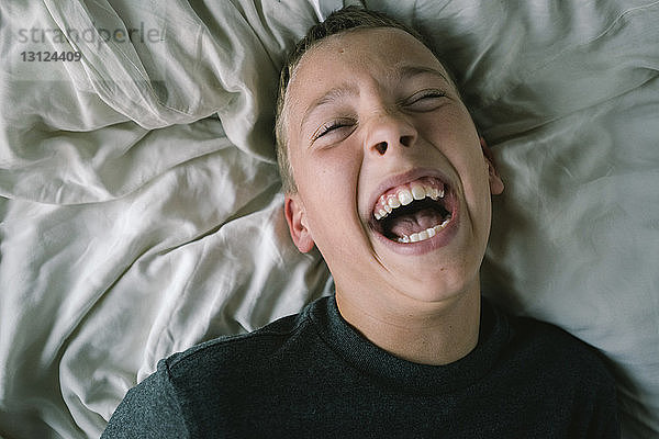Hochwinkelaufnahme eines Jungen  der lacht  während er zu Hause auf dem Bett liegt