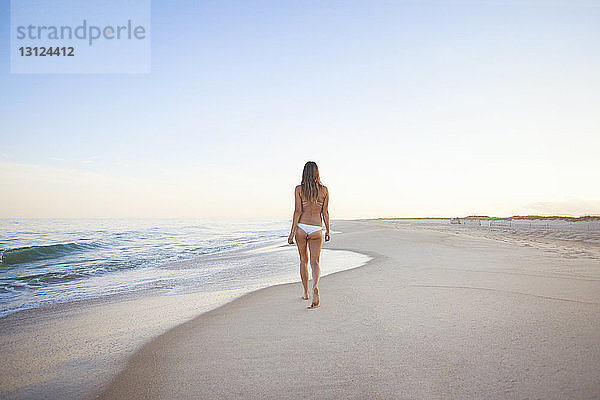 Rückansicht einer Frau  die bei klarem Himmel am Strand spazieren geht