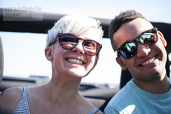 Porträt von lächelnden Freunden mit Sonnenbrille  die im Geländewagen gegen den Himmel fahren