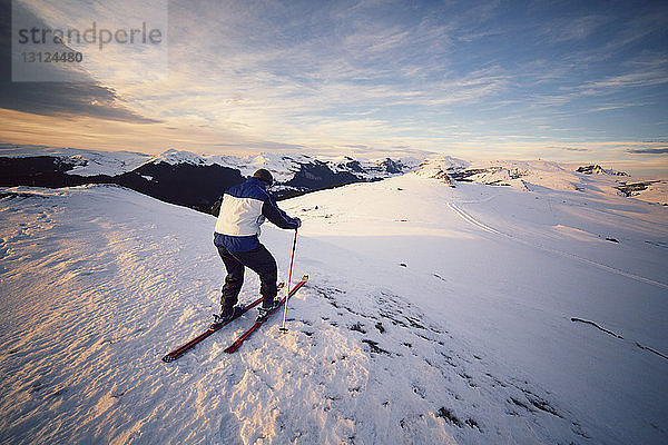 Rückansicht eines Mannes beim Skifahren auf einem schneebedeckten Berg gegen den Himmel