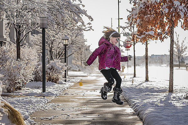 Glückliches Mädchen springt im Winter auf der Straße gegen den Himmel