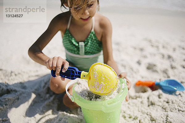 Mädchen spielt bei Sonnenschein mit Sandeimer und Schaufel am Strand