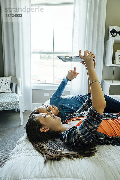 Mädchen zeigt auf Tablet-Computer  den die Schwester zu Hause im Bett hält