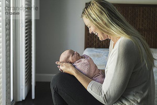 Seitenansicht einer glücklichen Mutter  die ihre neugeborene Tochter betrachtet  während sie sie zu Hause trägt