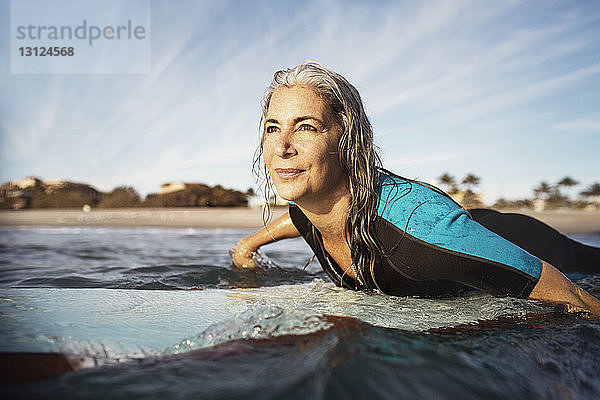 Reife Frau schaut beim Surfen auf See weg