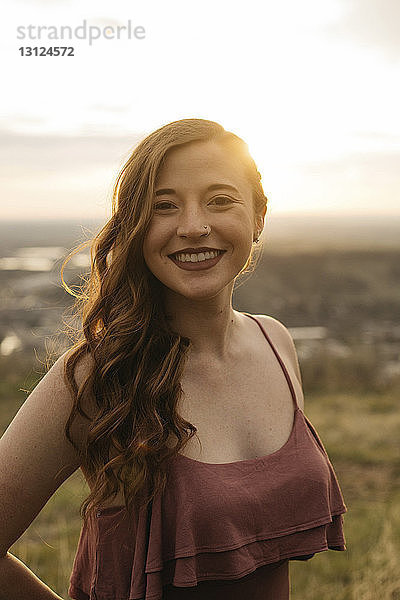 Porträt einer fröhlichen jungen Frau  die bei Sonnenuntergang auf dem Feld steht