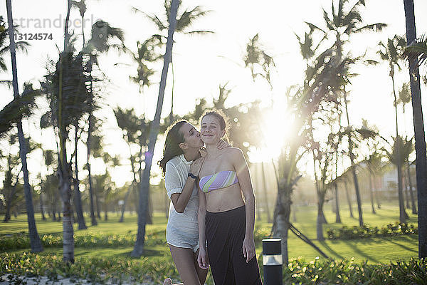 Frau umarmt Freundin  während sie an einem sonnigen Tag vor Palmen steht