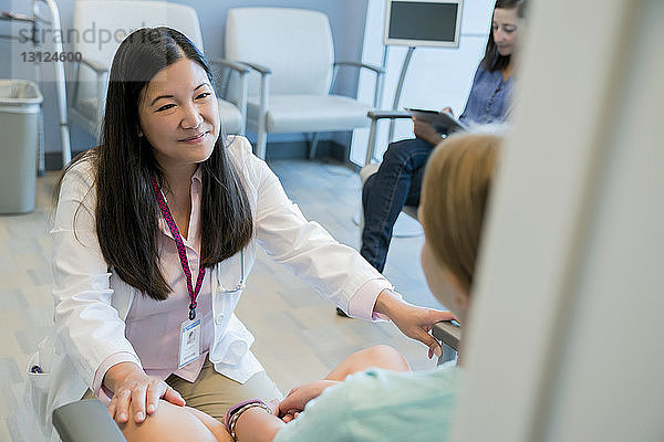 Hochwinkelansicht eines Kinderarztes  der mit der Patientin spricht  während die Frau im Hintergrund einen Tablet-Computer benutzt