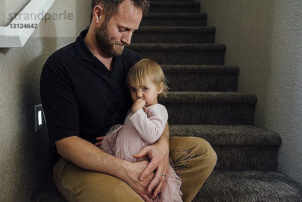 Porträt eines Mädchens  das mit seinem Vater zu Hause auf einer Treppe sitzt