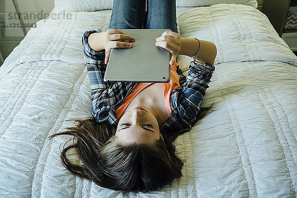 Teenager-Mädchen benutzt Tablet-Computer im Bett liegend