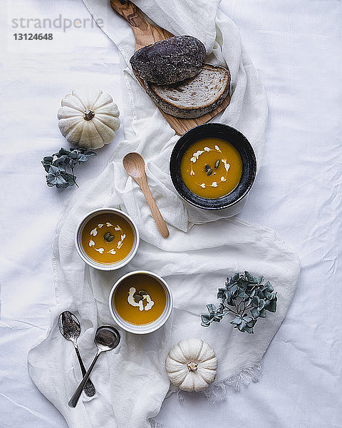 Draufsicht auf die in Schüsseln servierte Suppe mit Kürbissen und Broten auf Textil