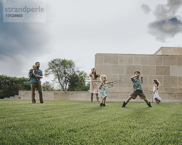 Vater schaut Kindern zu  die mit Hula-Hoop-Reifen auf dem Feld gegen den Himmel spielen