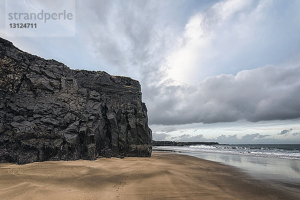 Felsklippe am Strand vor bewölktem Himmel