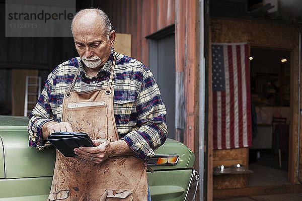 Leitender Handwerker benutzt digitales Tablett  während er vor der Werkstatt steht