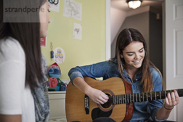 Frau übt Gitarre  während sie mit ihrer Schwester zu Hause sitzt