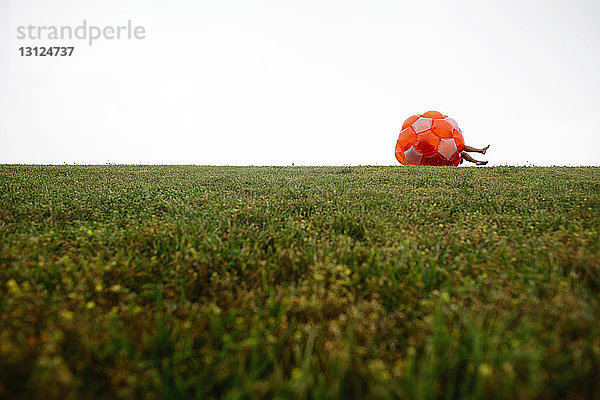 Mutter und Tochter rollen im Zorb-Ball auf einem Grasfeld vor klarem Himmel