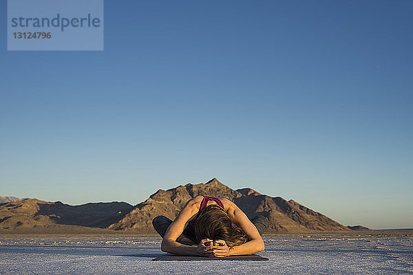 Frau trainiert  während sie bei Sonnenuntergang auf einer Matte vor klarem blauen Himmel sitzt