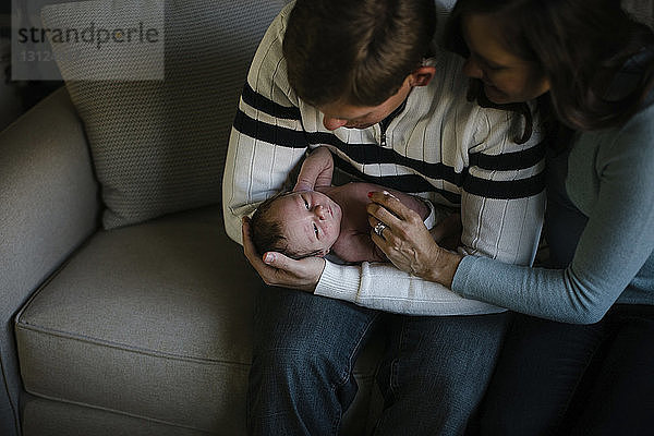 Hochwinkelaufnahme von Eltern  die mit ihrem neugeborenen Sohn spielen  während sie zu Hause auf dem Sofa sitzen
