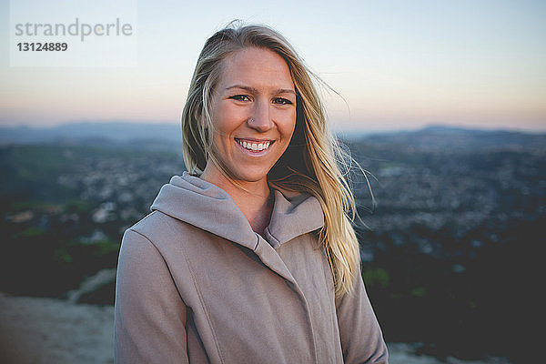 Porträt einer lächelnden Frau  die bei Sonnenuntergang auf einem Berg gegen den Himmel steht
