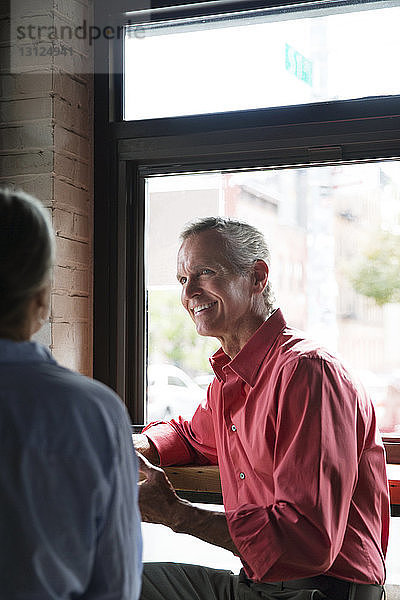 Lächelnder Mann sieht Frau an  während er im Café am Tisch sitzt