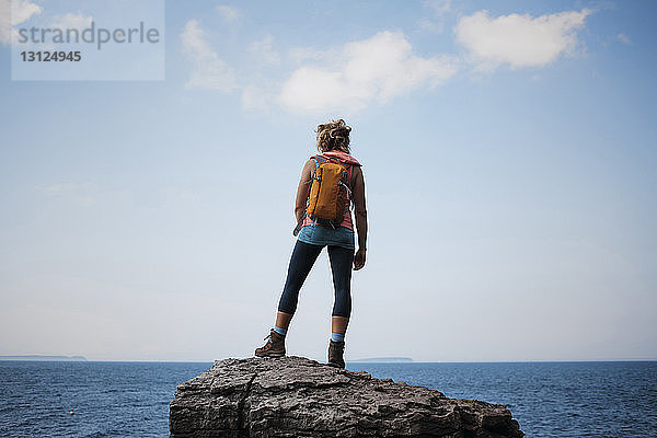 Rückansicht einer Wanderin mit Rucksack auf Fels stehend gegen Meer und Himmel im Bruce Peninsula National Park