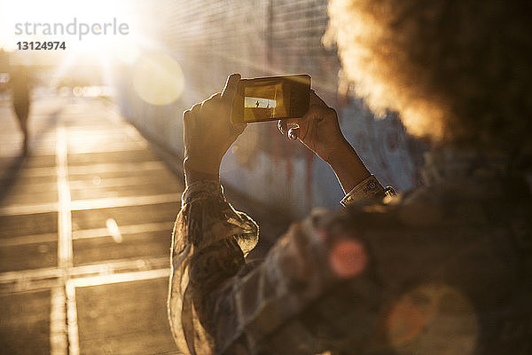 Ausschnitt einer Frau  die an einem sonnigen Tag per Handy fotografiert