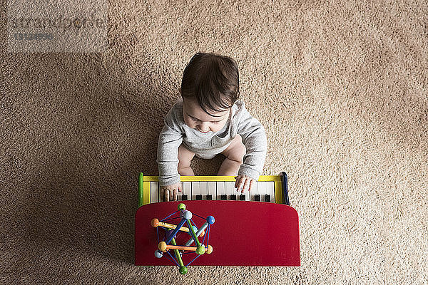 Draufsicht auf einen kleinen Jungen  der zu Hause auf einem Teppich Spielzeugklavier spielt