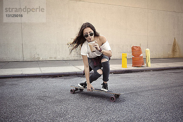 Junge Frau trinkt Saft beim Skateboarden auf der Straße