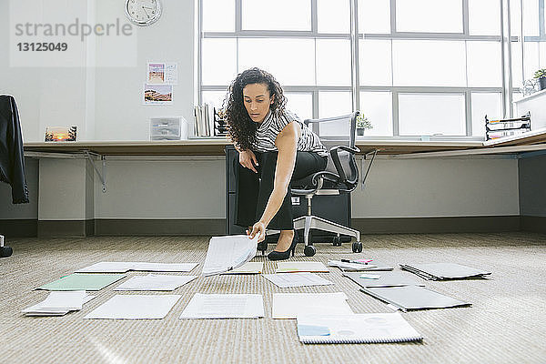 Geschäftsfrau ordnet Dokumente auf dem Boden im Büro an