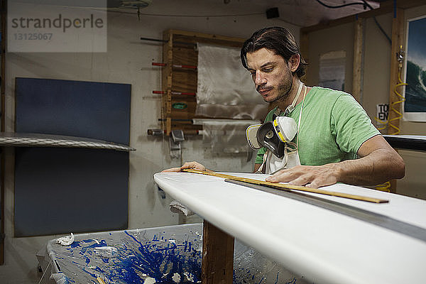 Konzentrierter männlicher Arbeiter misst Surfbrett in Werkstatt