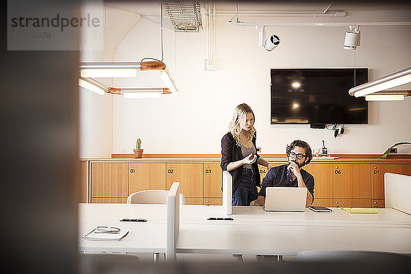 Geschäftsmann benutzt Laptop-Computer während einer Diskussion mit einer Mitarbeiterin im Büro