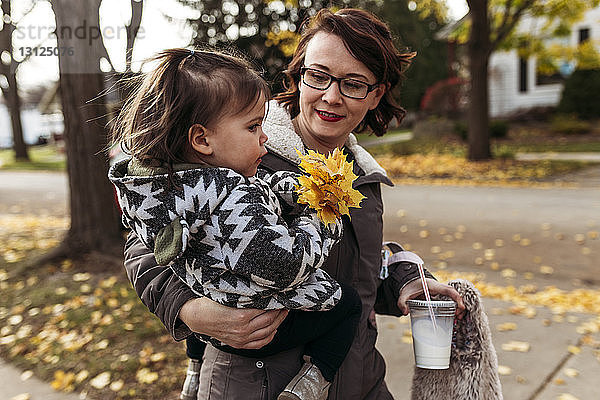 Mutter trägt Tochter  während sie im Park Einwegglas hält
